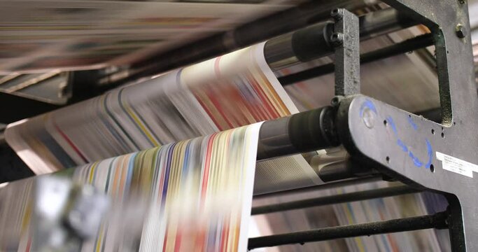 Left to right panning shot - newspaper printing process - reams of freshly printed newspapers speed through the rollers on their way to to be cut - information, news and media concepts.