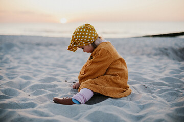 Funny child in oriental dress sitting on beach sand and playing with sand