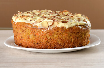 Carrot cake with almonds, and cheese sauce topping on a white plate.