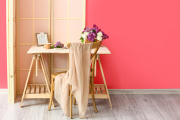 Modern workplace with basket and lilac flowers near color wall