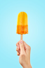Woman holds yellow ice cream on blue background. Color frozen fruit popsicle.