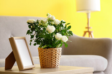 Beautiful white roses in pot and frame on table in room