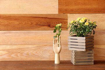Hand and boxes with yellow roses on table near wooden wall