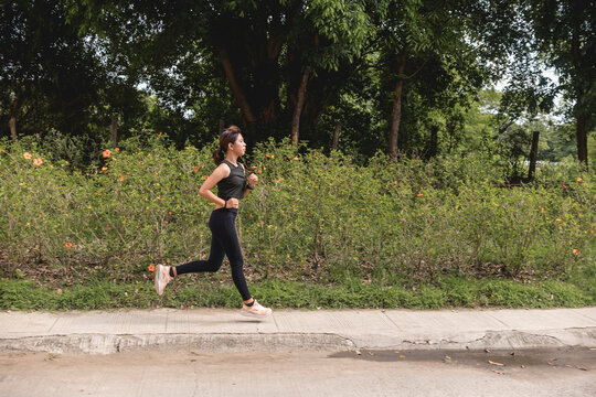A young asian woman running along the sidewalk of a park. Cardio workout, 5k or marathon endurance training.