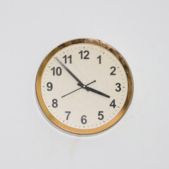 large round clock with an old, simple design and a gold frame hanging in a white wall showing accurate time