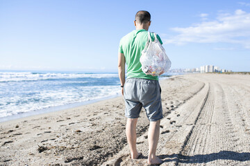 Man walking at beach with net bag picking plastic bottles
