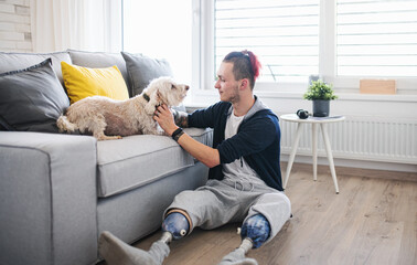 Portrait of disabled young man playing with dog indoors at home, leg prosthetic concept.