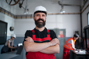 Portrait of worker with helmet indoors in factory looking at camera.