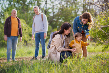 Small toddler with parents and grandparents on a walk outdoors in nature.
