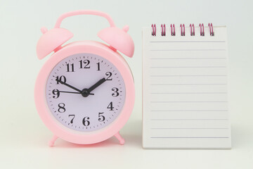 Pink alarm clock and blank notepad page on gray background, mock up.