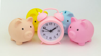 Pink alarm clock and many piggy banks. Save money, choosing savings fund concept.