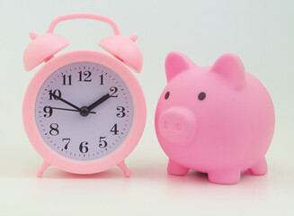 Pink alarm clock and piggy bank. Save money and time concept.