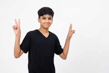 Enthusiastic young India boy raises his fingers showing victory sign. Cute teenager raising his arms in delight