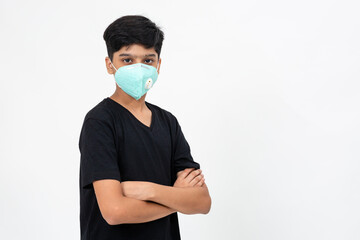 Young Indian boy wears face mask for protection against Covid-19. Cute teenager standing with arms crossed.