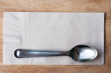 Stainless tea spoon on brown tissue, coffee spoon on wooden table.