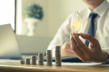 Hand of a businessman Innovative and inspired by light bulbs and coins, Calculating financial...