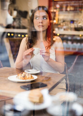 Portrait of young female at table in a cafe, drinking coffee from a cup