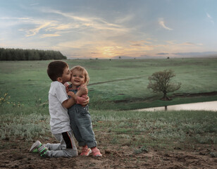 The elder brother kisses his little sister against the backdrop of a picturesque landscape.