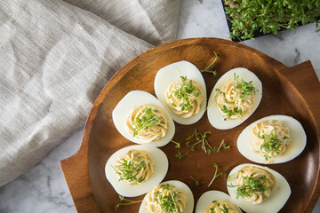 Kalte gefüllte russische Eier mit Frischkäse, Kresse und Kräuter farciert auf Holz Eierteller, Leinen Tuch und Marmor Hintergrund hell zu Ostern, Büffet, Snack oder Vorspeise