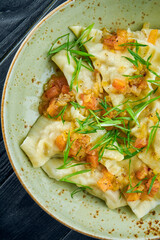 Traditional dish of Israeli cuisine - chicken kreplach with tomato salsa and green onions in a plate on a black wooden background. Restaurant food. Dumplings with different fillings