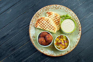 A Appetizing oriental dish, falafel with pita bread, served with white sauce and pickles in a green plate against a dark, woody background. Vegetarian food