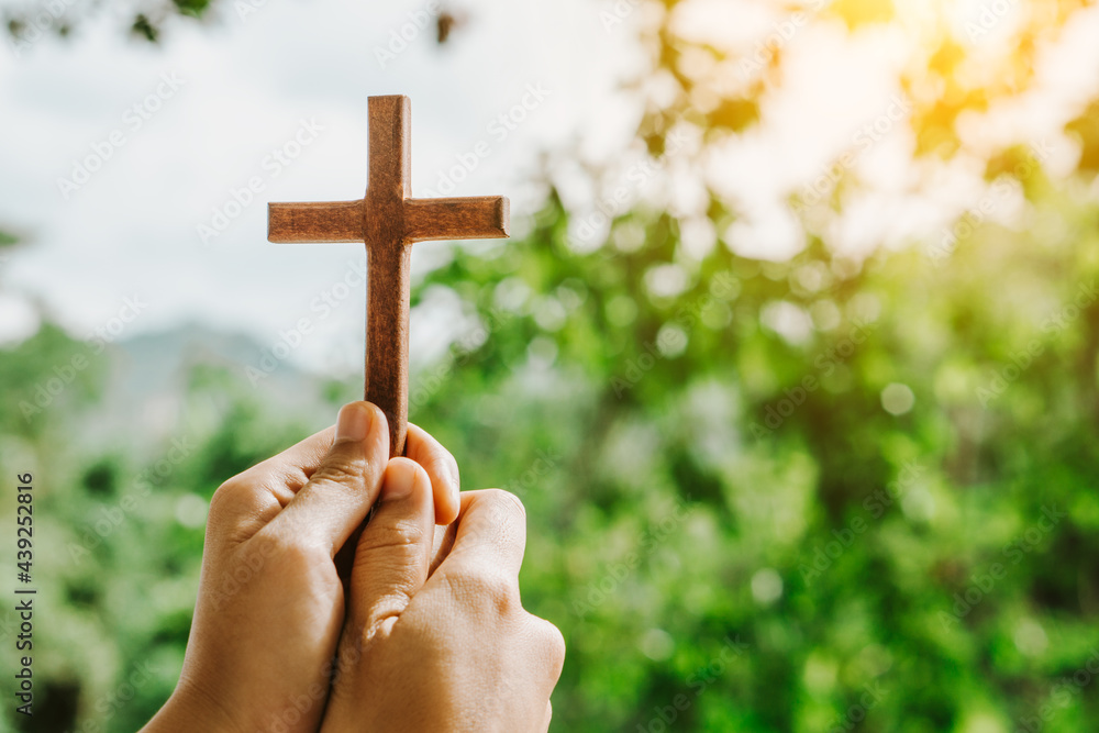 Wall mural man praying with cross in nature sunrise background, symbol of faith.