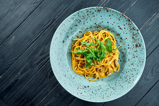 Delicious Italian carbonara pasta with bacon and raw yolk, parmesan and rucola. Homemade pasta served in a blue plate on a dark background