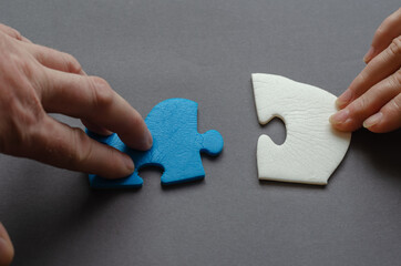 People hold a blue and white puzzle piece against a gray background. Man and woman with unconnected puzzle pieces.