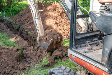 Mini excavator digs the ground. Trench for water pipes or communication lines