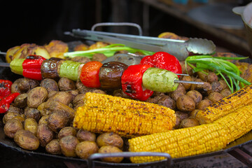 Healthy street food to go, on small potatoes, red bell pepper, yellow corn cobs, green onion feathers. Delicious food cooked over an open fire, which is offered at a street food fair, event.