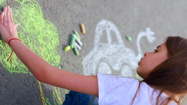 Little girl with creative craft hobby drawing electro on the asphalt with chalk car environment, eco friendly, save energy in park at summer day