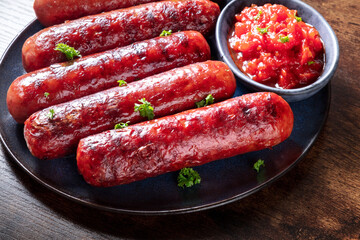 Grilled sausages with ketchup, a close-up shot on a dark rustic wooden table. Wiener Bratwurst portion on a plate