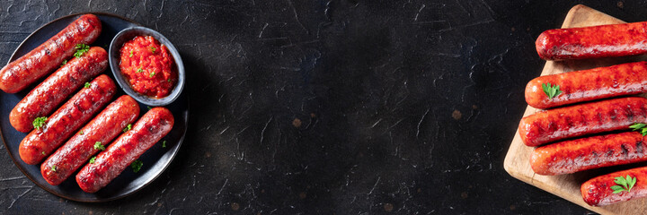 Sausages panorama with copy space, top shot on a black slate background. Delicious bbq meal