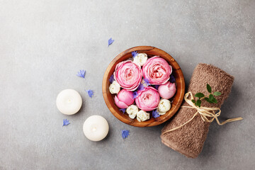 Beauty, aromatherapy and spa background with perfumed water with flowers in wooden bowl, towel and candles on stone table. Top view, flat lay.