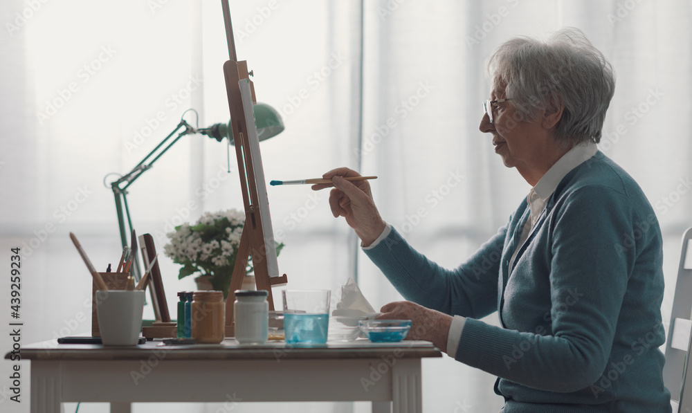 Wall mural senior woman sitting at desk and painting