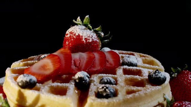 4K Close up pour honey syrup on freshly baked waffles. Decorating toping with mayple syrup, fresh strawberry, strawberry slice thin, blueberry, and icing sugarmade straight from the oven.