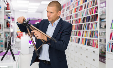 Buyer carefully chooses a tripod for the camera in an electronics store