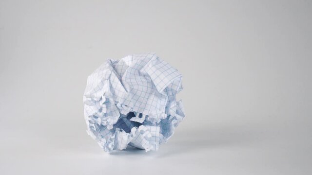 Thrown crumpled paper ball falls and rolls on a white surface in slow motion. Search for ideas and brainstorming concept