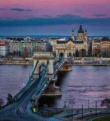 Photo sur Plexiglas Széchenyi lánchíd Budapest, Hungary - The famous Szechenyi Chain Bridge (Lanchid) at sunset decorated with national flags celebrating the 15th of March 1848 civic revolution day. St.Stephen's Basilica and magenta sky