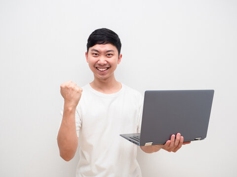 Asian man white shirt hold laptop in hand and fist up with happy smile on his face onm white background