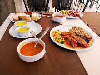 White plates with food on the table in a Turkish hotel restaurant. Tomato soup, rice with stewed vegetables and dessert on a buffet