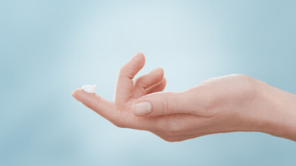 Female skin care model lifts her hand with a drop of cream on forefinger up and down twice against...