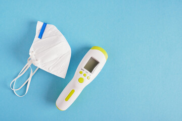 white KN95 or N95 face mask on blue background. Surgical protective mask and digital thermometer