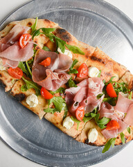 Pinza with vegetables and meat cooked in an oven with wood and served on a metal tray over white background.
