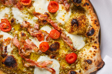 Pizza napoletana con pesto di basilico, pomodori, pancetta e mozzarella