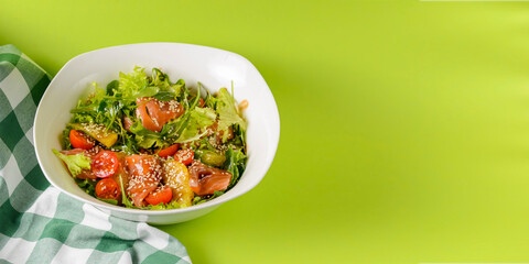 Fresh salad with salmon and vegetables close up in a bowl over bright green background with tablecloth.