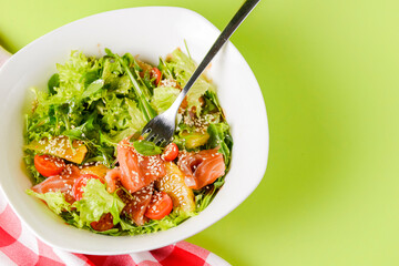 Fresh salad with salmon and vegetables close up in a bowl over bright green background with tablecloth.