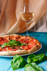 Fresh italian pizza with salami and black olives served with a glass of white wine.