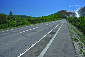 青空の下、水蒸気を上げる山に向かって走る直線路。