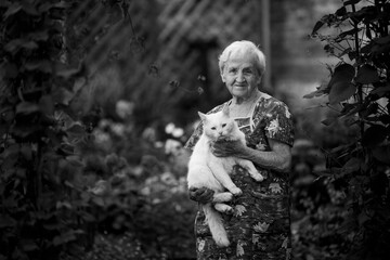 Old woman in the garden with her white cat. Black and white photo.